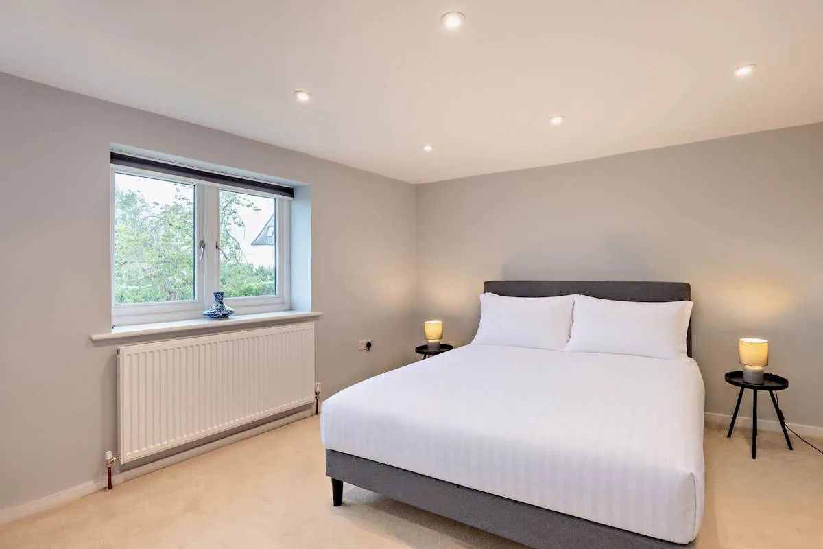 A bedroom with a double bed, bedside tables, and a window.