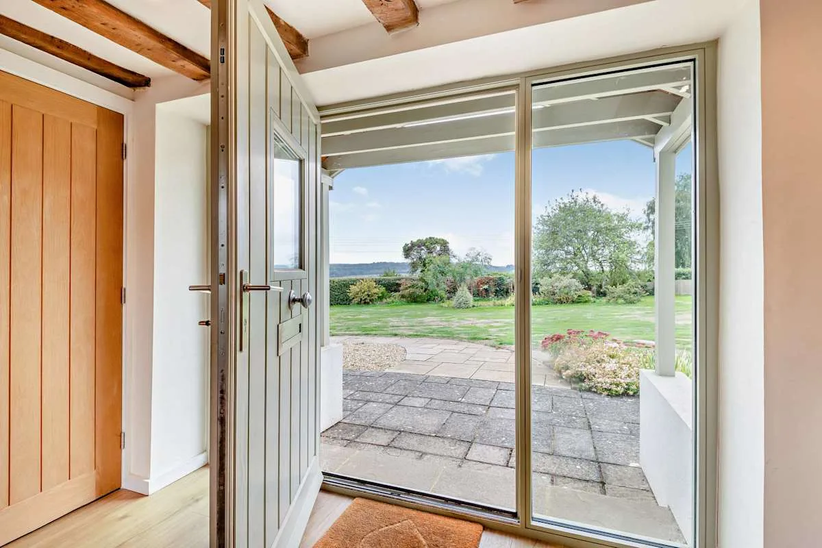 An open doorway leads to a paved patio overlooking a green garden.