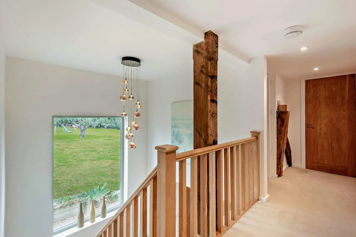 A bright stair landing with a wooden railing and a large window overlooking greenery.