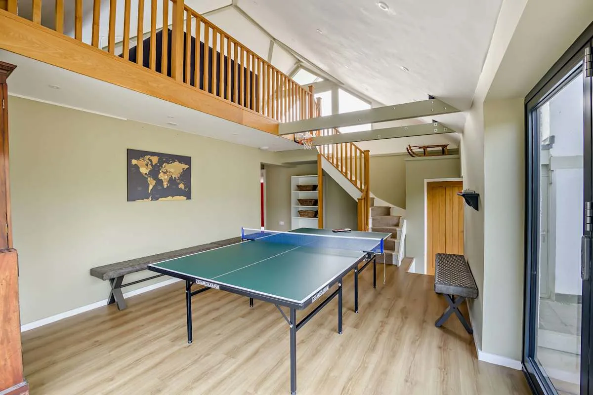 A bright recreation room with a table tennis table beneath an open upper-level railing.