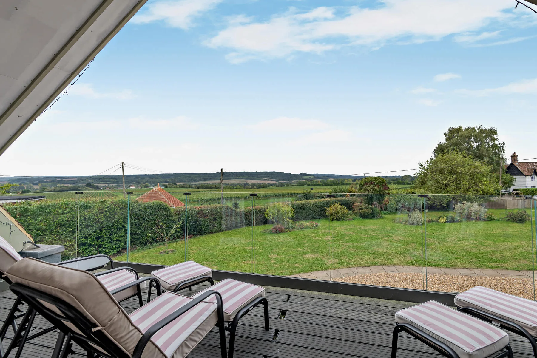 A deck with cushioned loungers overlooks a grassy garden and open countryside.