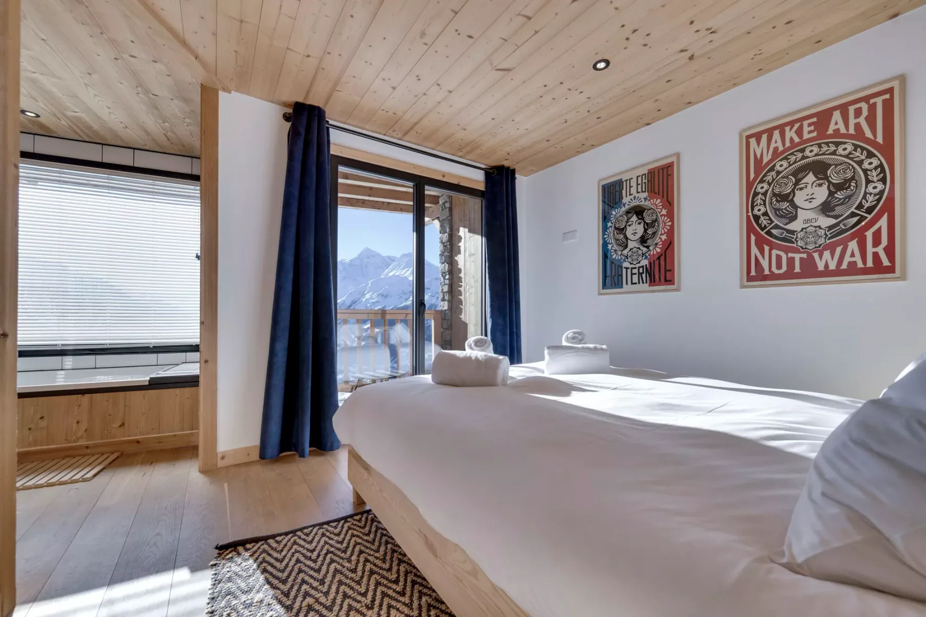 Un dormitorio con una cama, grandes ventanas y arte colorido en las paredes.