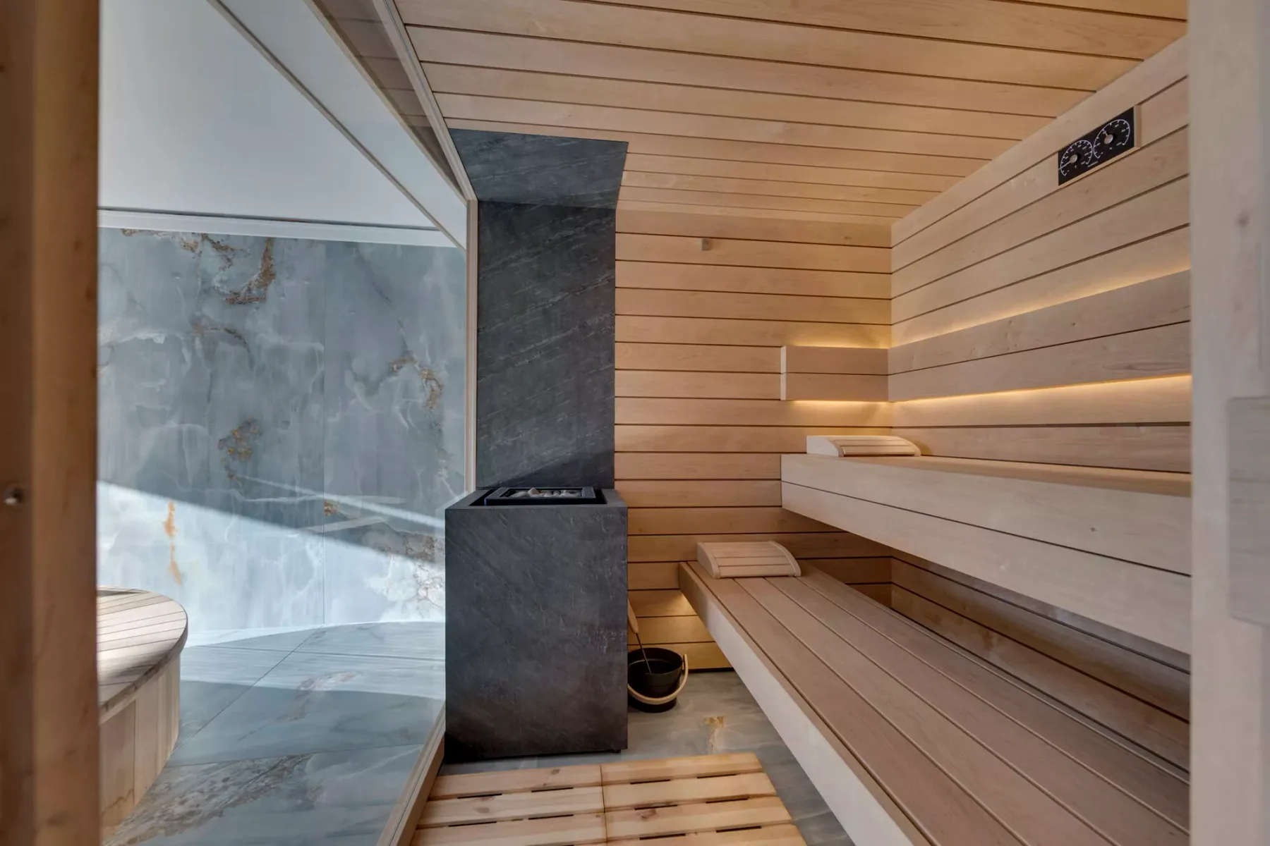 Una sauna revestida de madera, con asientos escalonados y una estufa oscura en el centro.