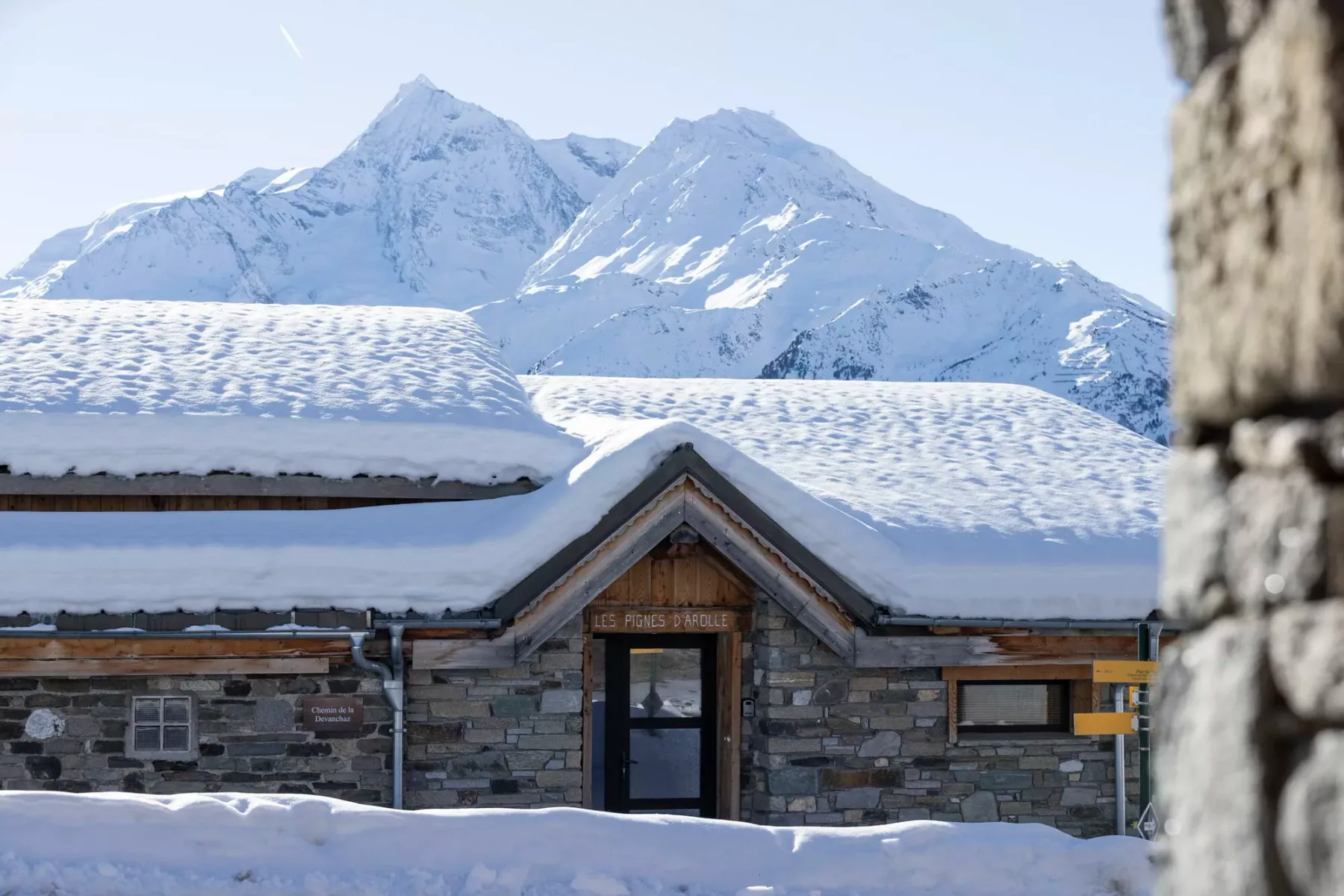 Un edificio de piedra cubierto de nieve se alza frente a montañas nevadas.