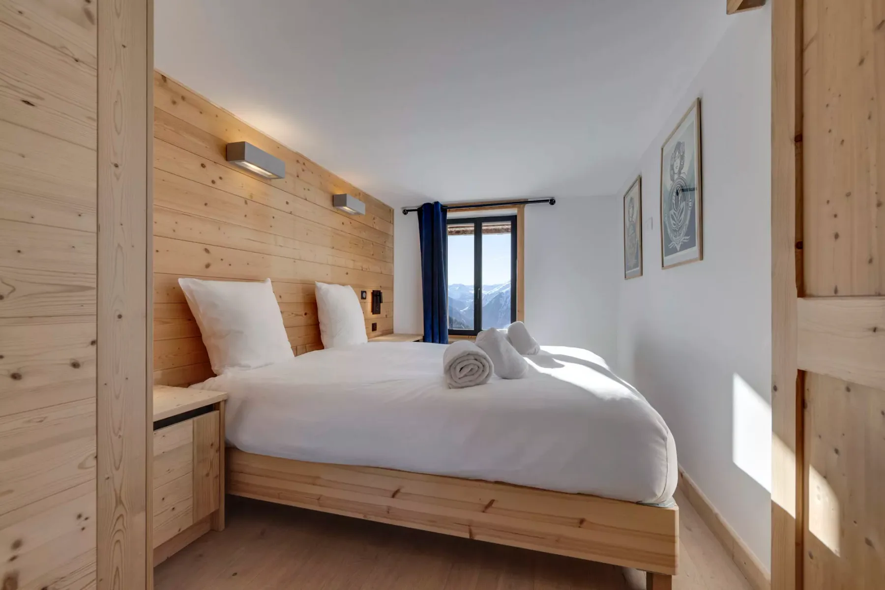 Un dormitorio con una cama vestida de blanco y una ventana con vistas a las montañas.
