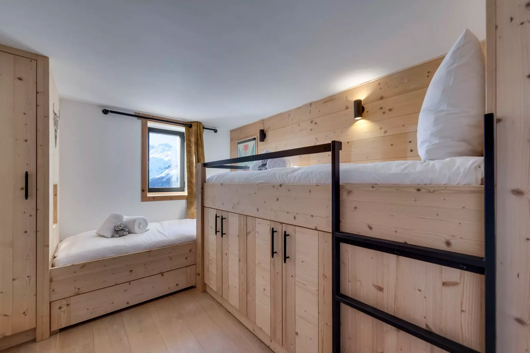 Un dormitorio con una cama elevada de madera y una cama pequeña bajo una ventana.