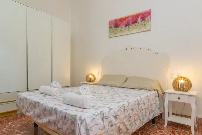 Un dormitorio con colcha floral, cabecero claro y lámparas de mesita.