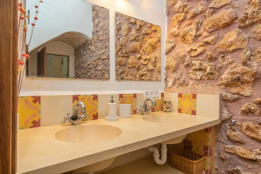 Un tocador de baño con dos lavabos está bajo espejos, junto a paredes de piedra.