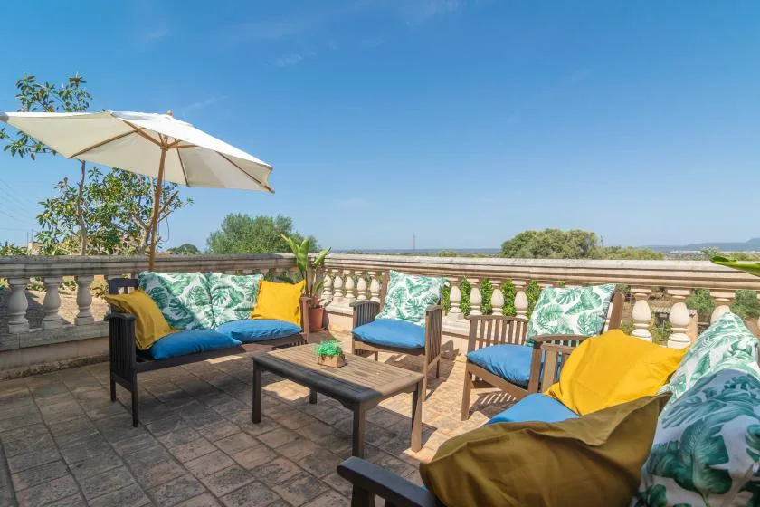 Una terraza soleada con asientos al aire libre y una sombrilla da al paisaje.