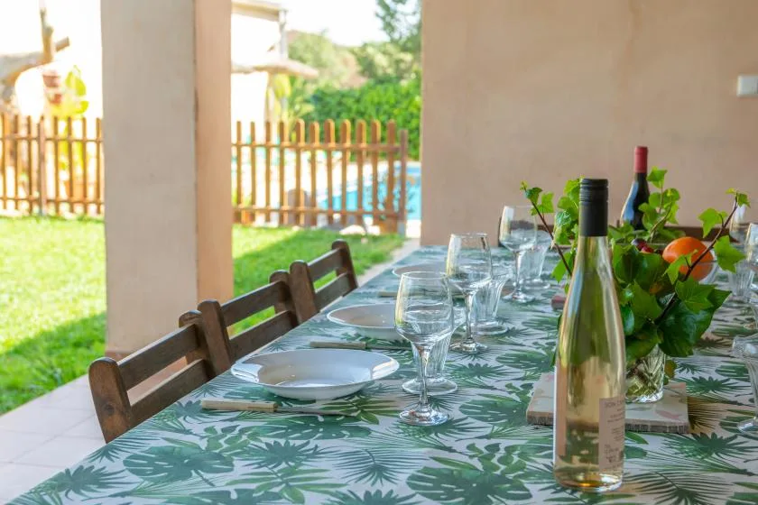 Una mesa de comedor puesta al aire libre da a un jardín y una piscina.