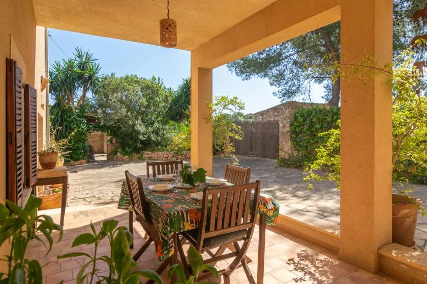 Un comedor exterior cubierto con mesa y sillas se abre a un patio con jardín.