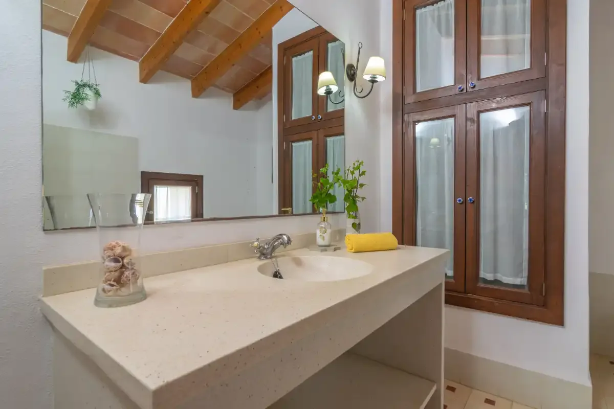 Un lavabo de baño con espejo está junto a ventanas altas.