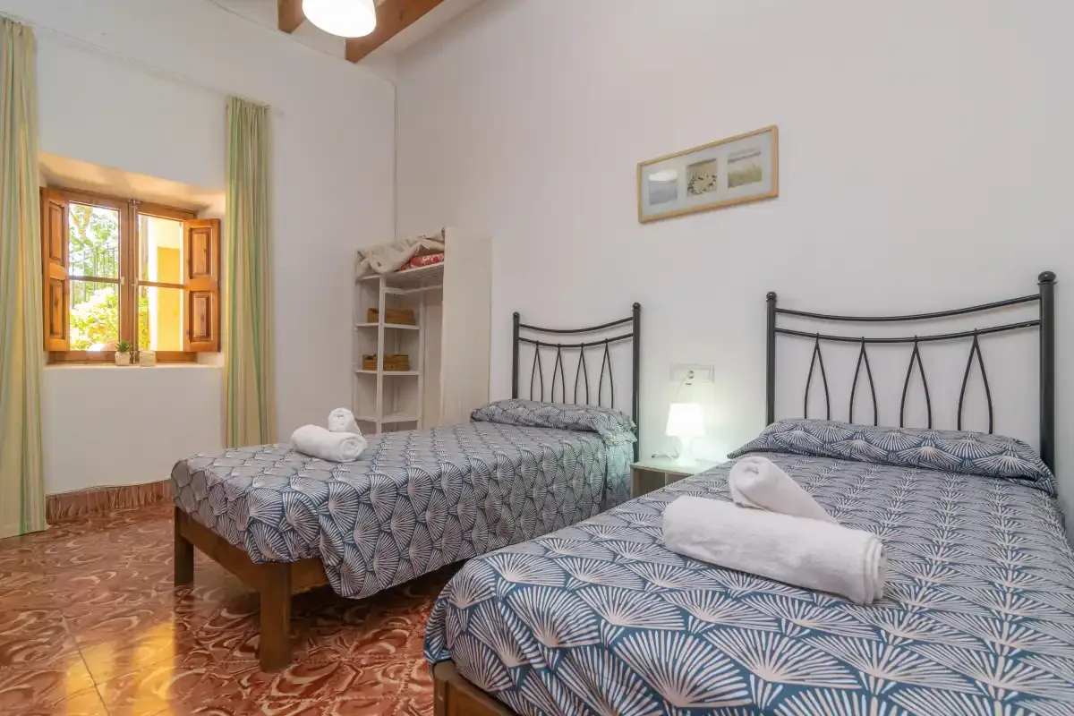 Un dormitorio con dos camas, ropa de cama estampada y una ventana soleada.