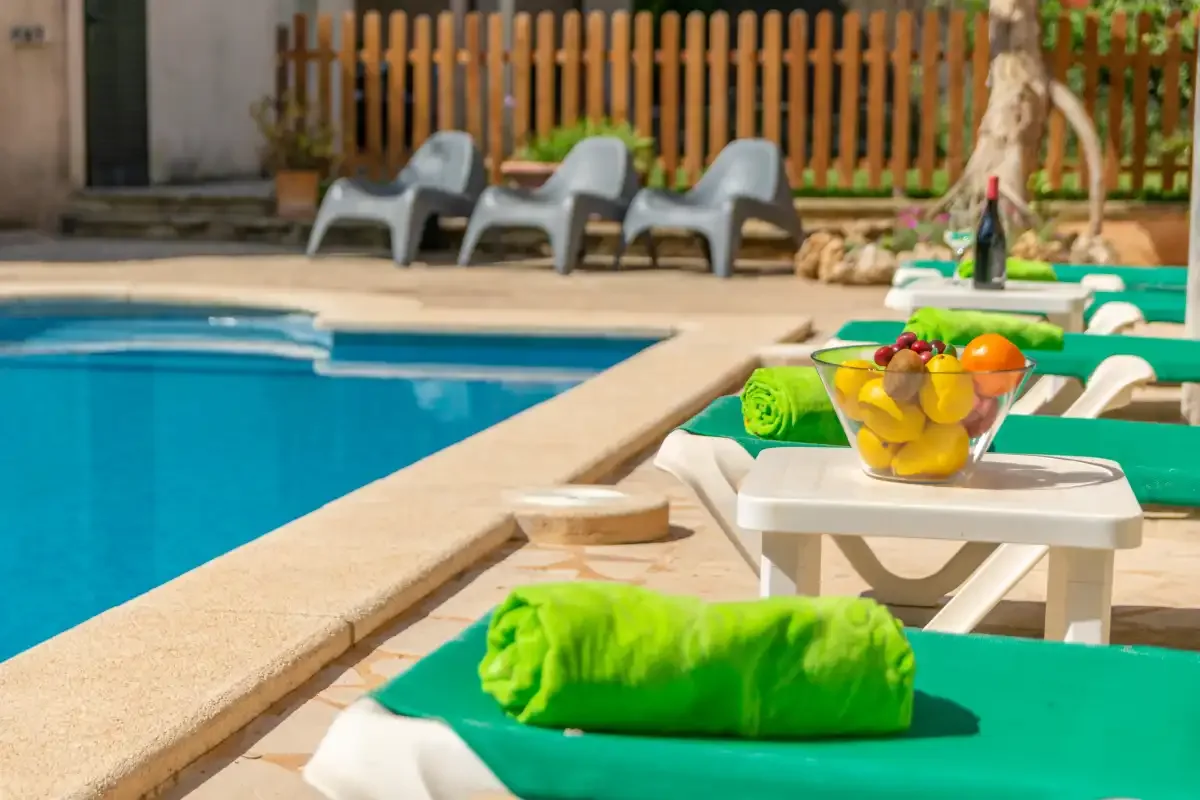 Una piscina está rodeada de tumbonas y una pequeña mesa con fruta.