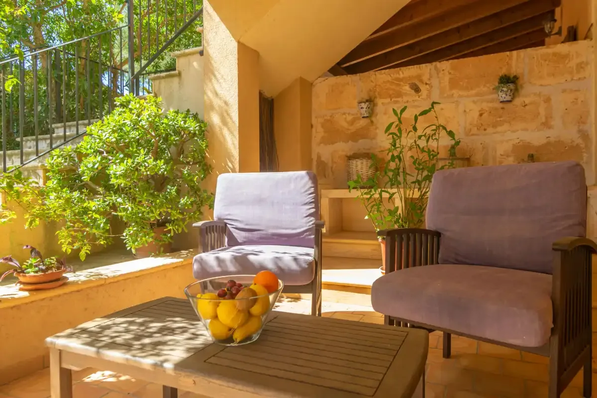 Una zona exterior de estar a la sombra con sillones acolchados y una mesa baja.