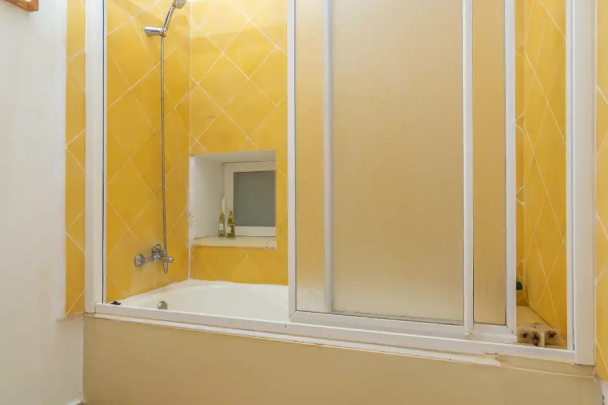 Una ducha con paredes de azulejos amarillos y un panel de vidrio esmerilado.