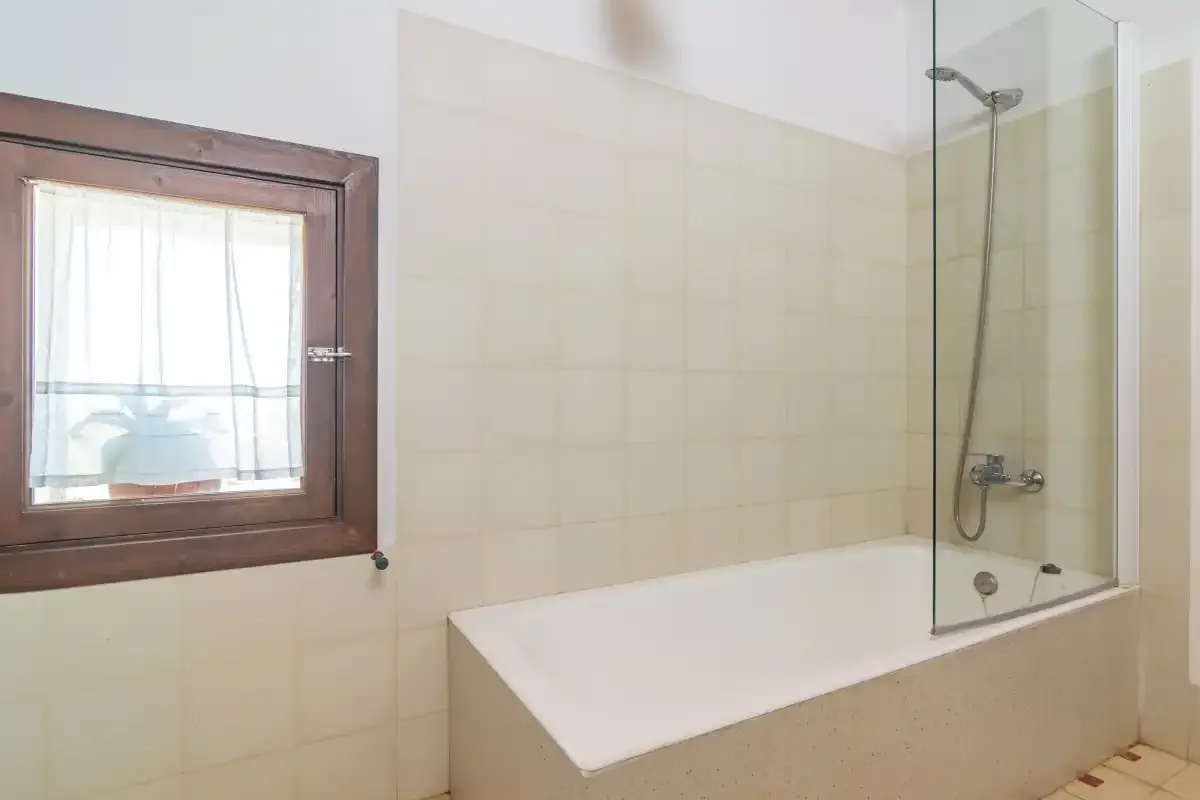 Un baño alicatado con bañera y ducha junto a una ventana.