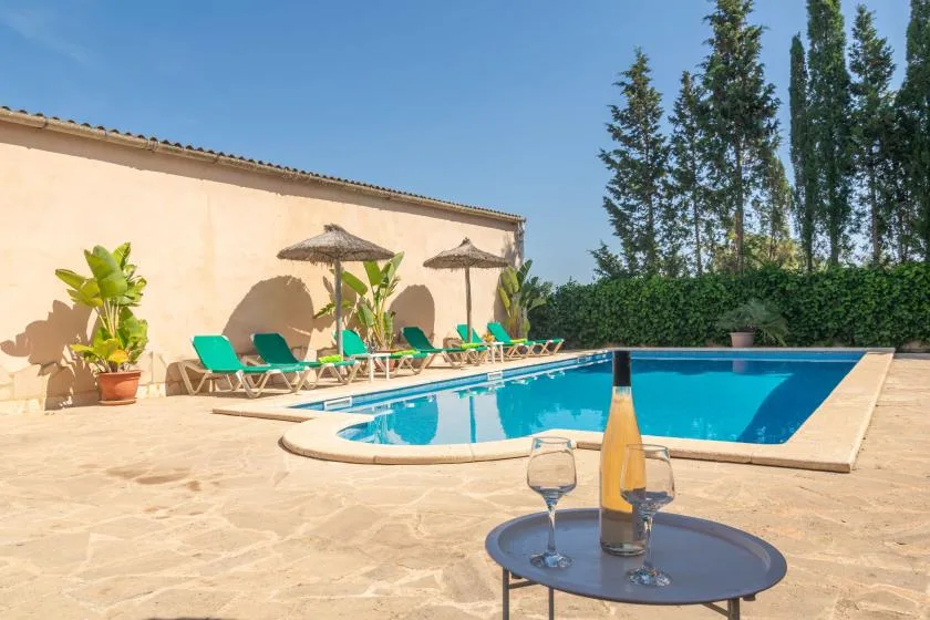 Una piscina al aire libre junto a un patio soleado con asientos y sombrillas.