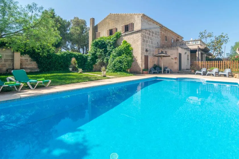 Una piscina al aire libre junto a una casa de piedra y un jardín.