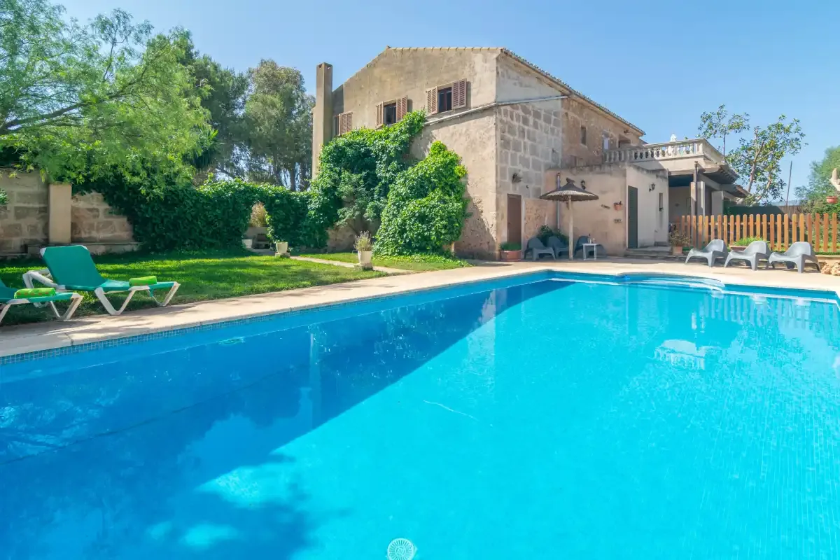 Una piscina junto a un edificio de piedra, con asientos de descanso junto a la terraza.