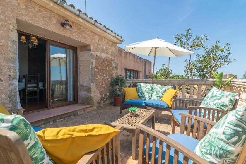 Una terraza soleada con asientos, cojines de colores y una gran sombrilla.