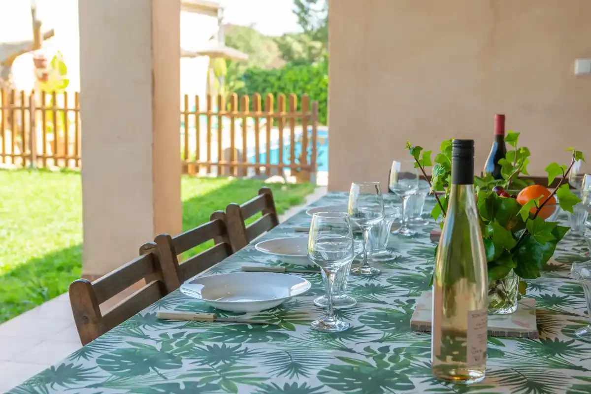 Una mesa de comedor en un patio cubierto está puesta con platos, copas y plantas.