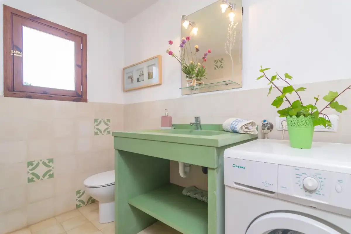 Un baño con mueble de lavabo verde, espejo y lavadora.
