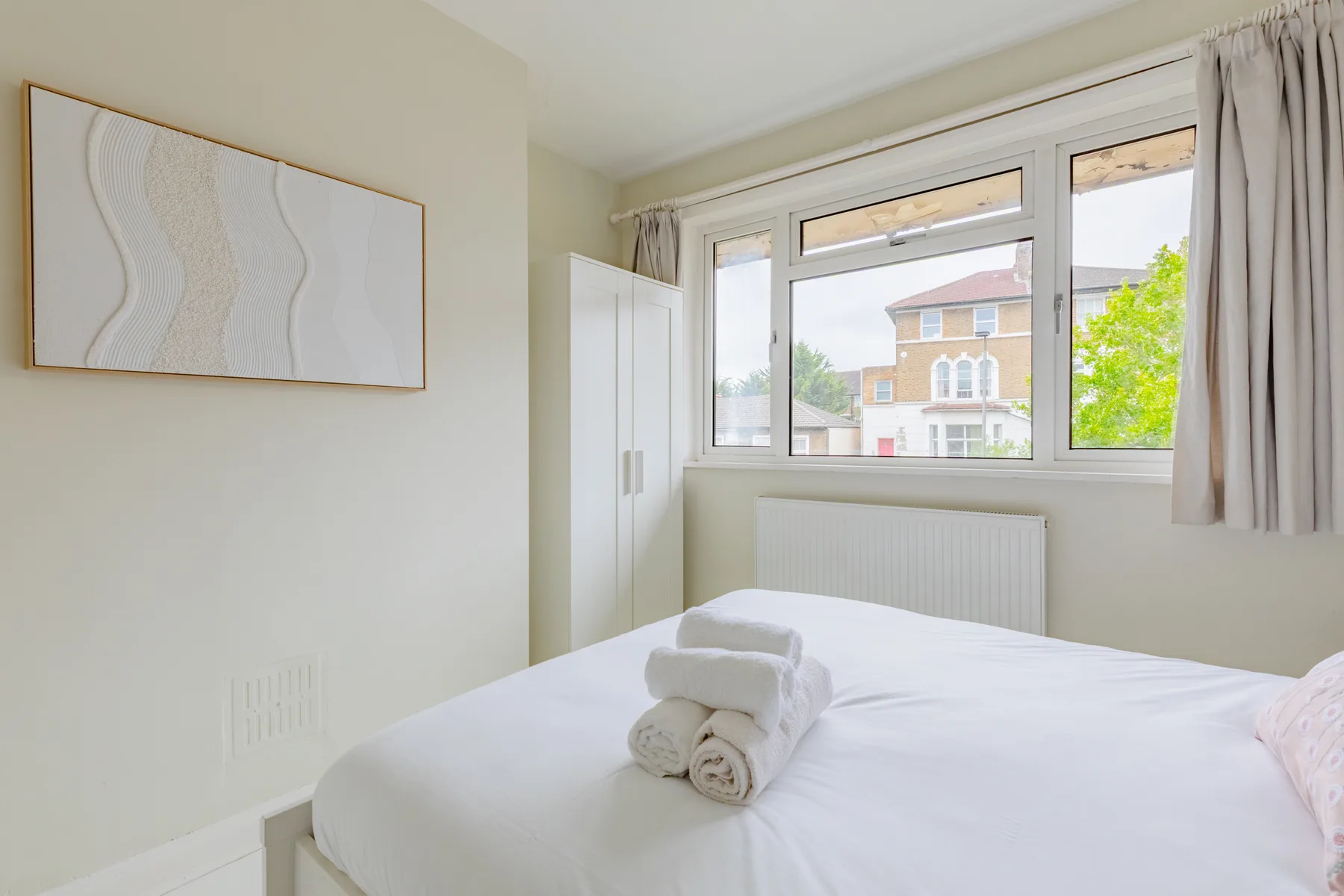 A bright bedroom with a bed, folded towels, and a large window.