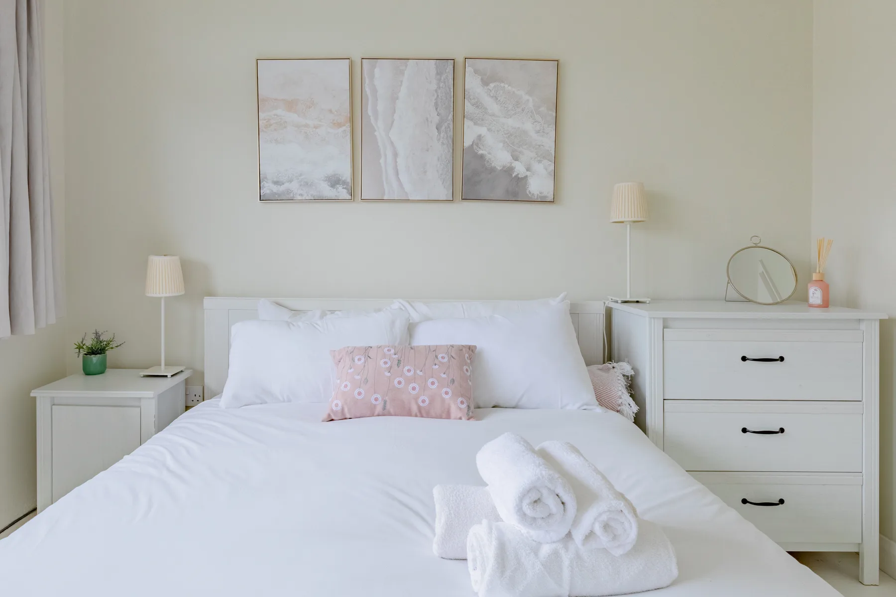 A bright bedroom with a neatly made bed and framed artwork above it.