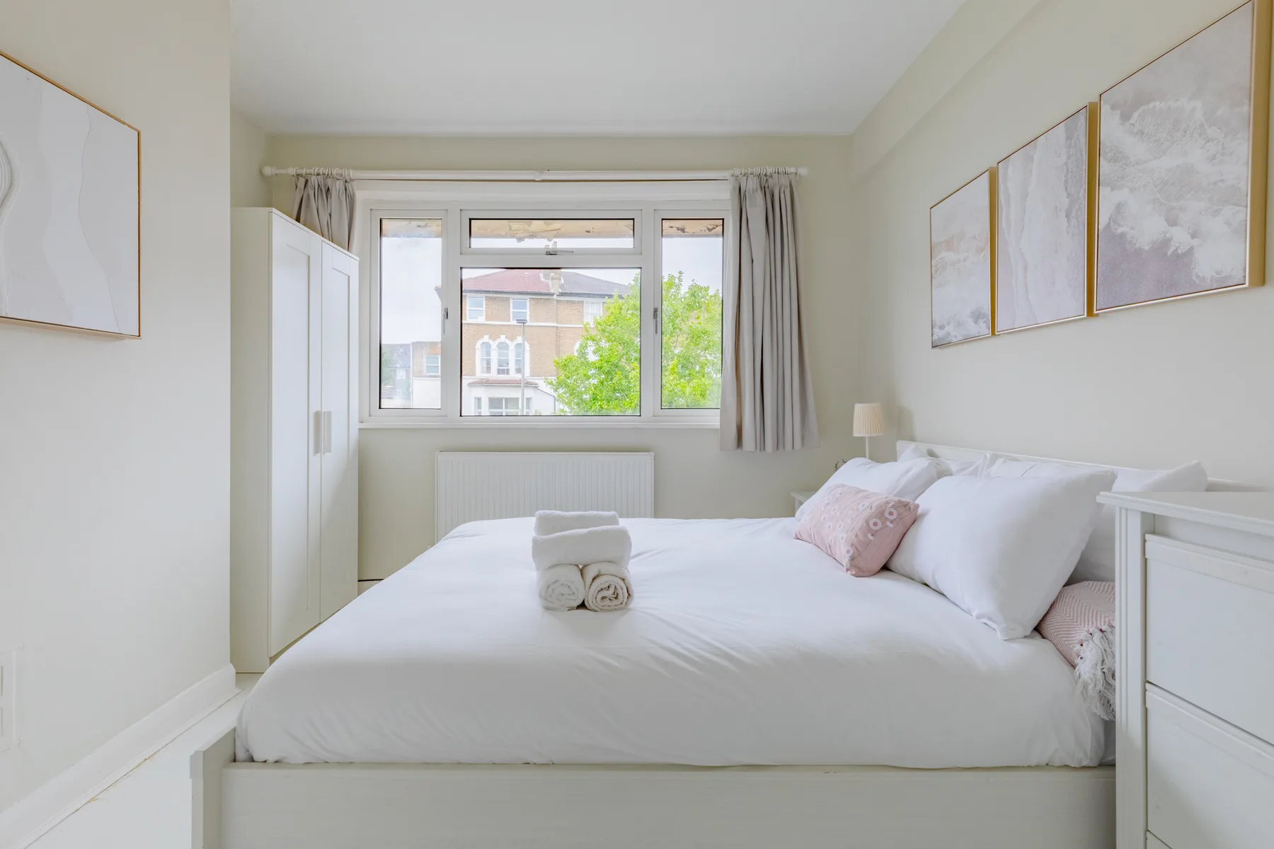 A bright bedroom with a neatly made bed and a window overlooking trees.