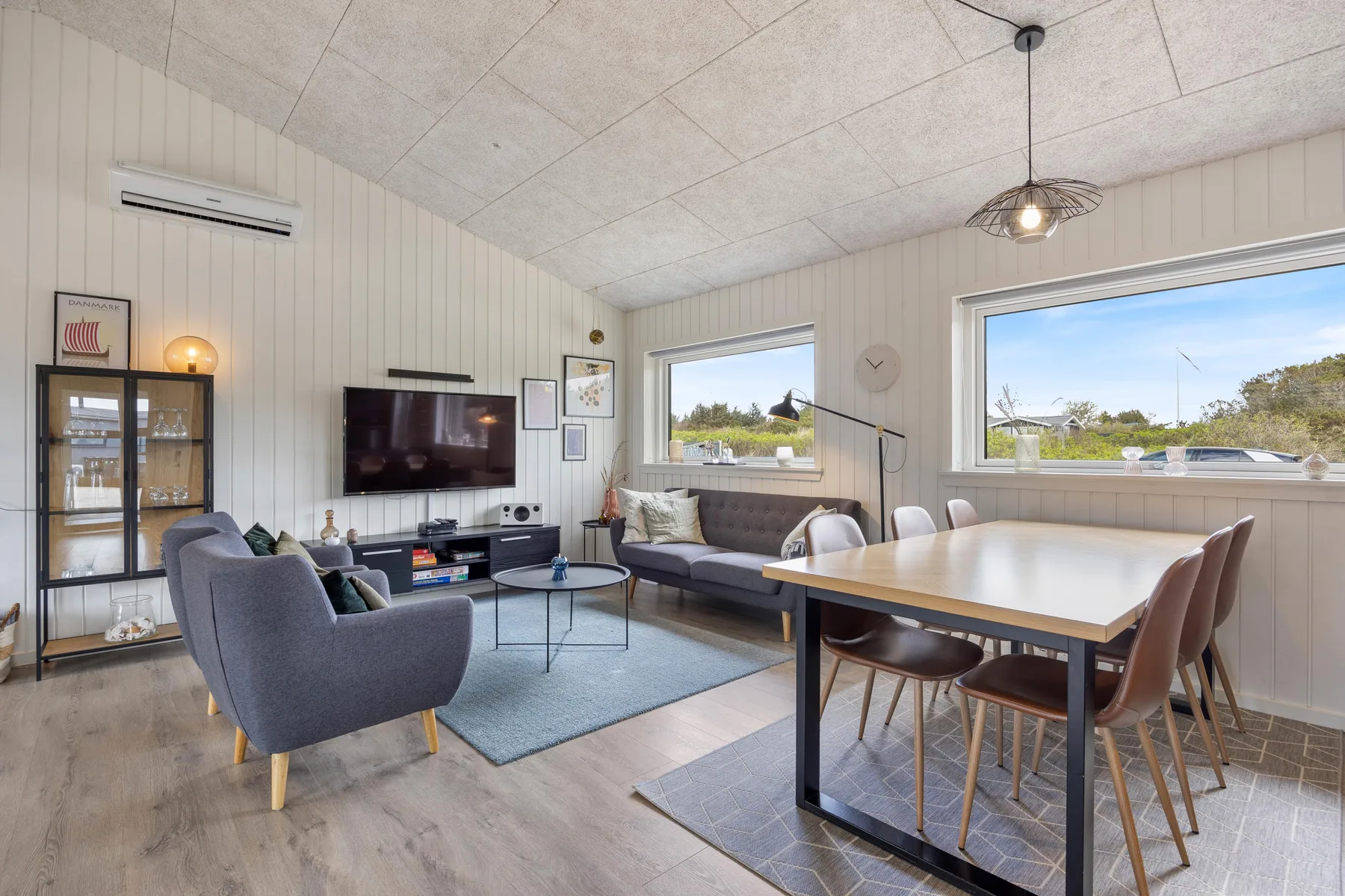 A bright living and dining area with large windows and a television.