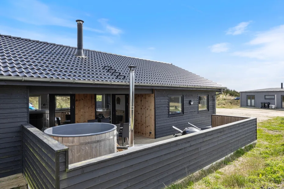 A dark-sided house with a fenced patio and a round outdoor hot tub.