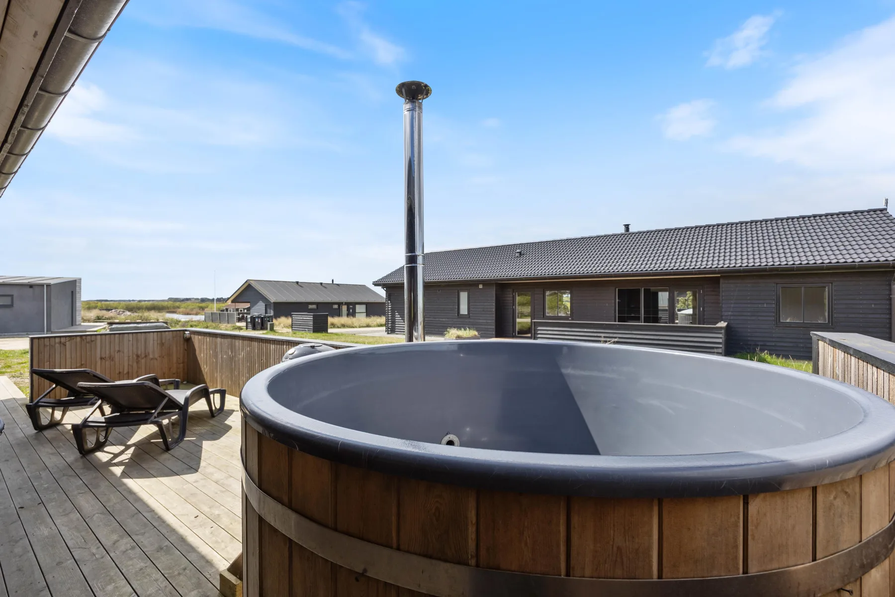 An outdoor hot tub sits on a wooden deck beside a modern house.