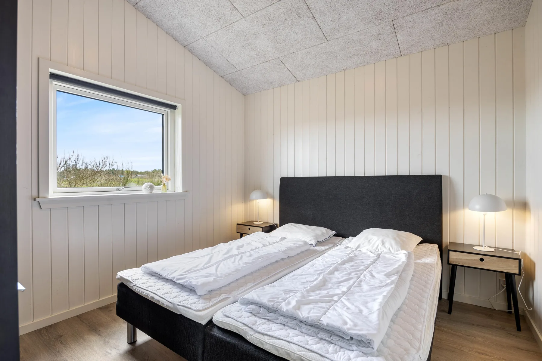 A bedroom with a double bed and a window overlooking greenery.