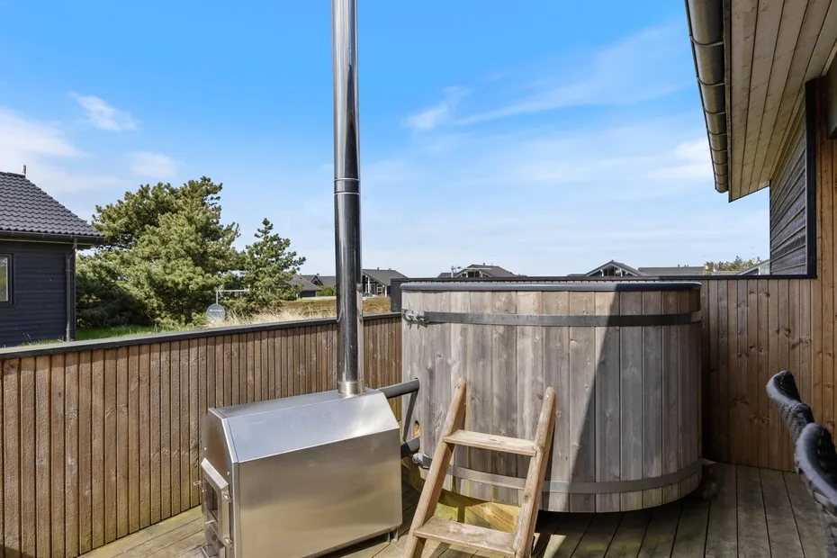 An outdoor wooden deck features a round hot tub and a metal grill.