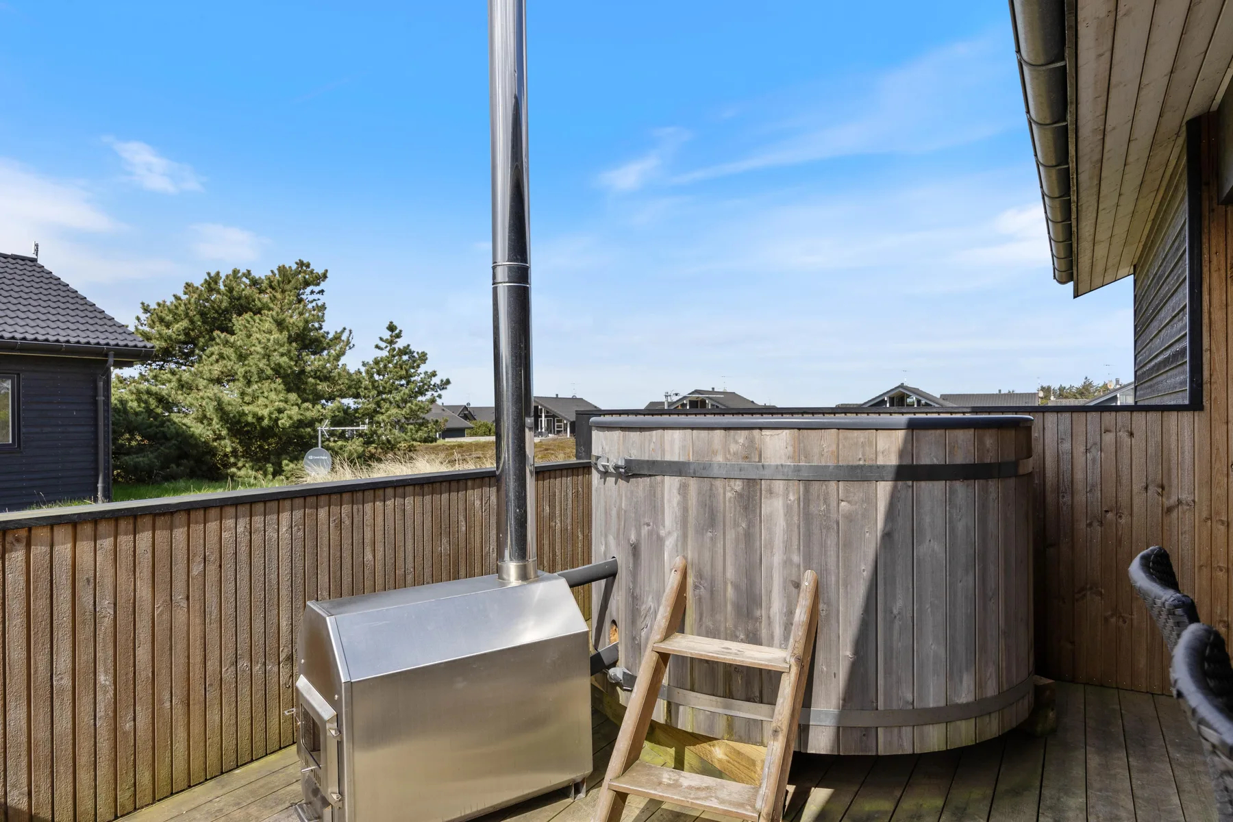 A wooden deck with a round hot tub and metal grill beside the house.