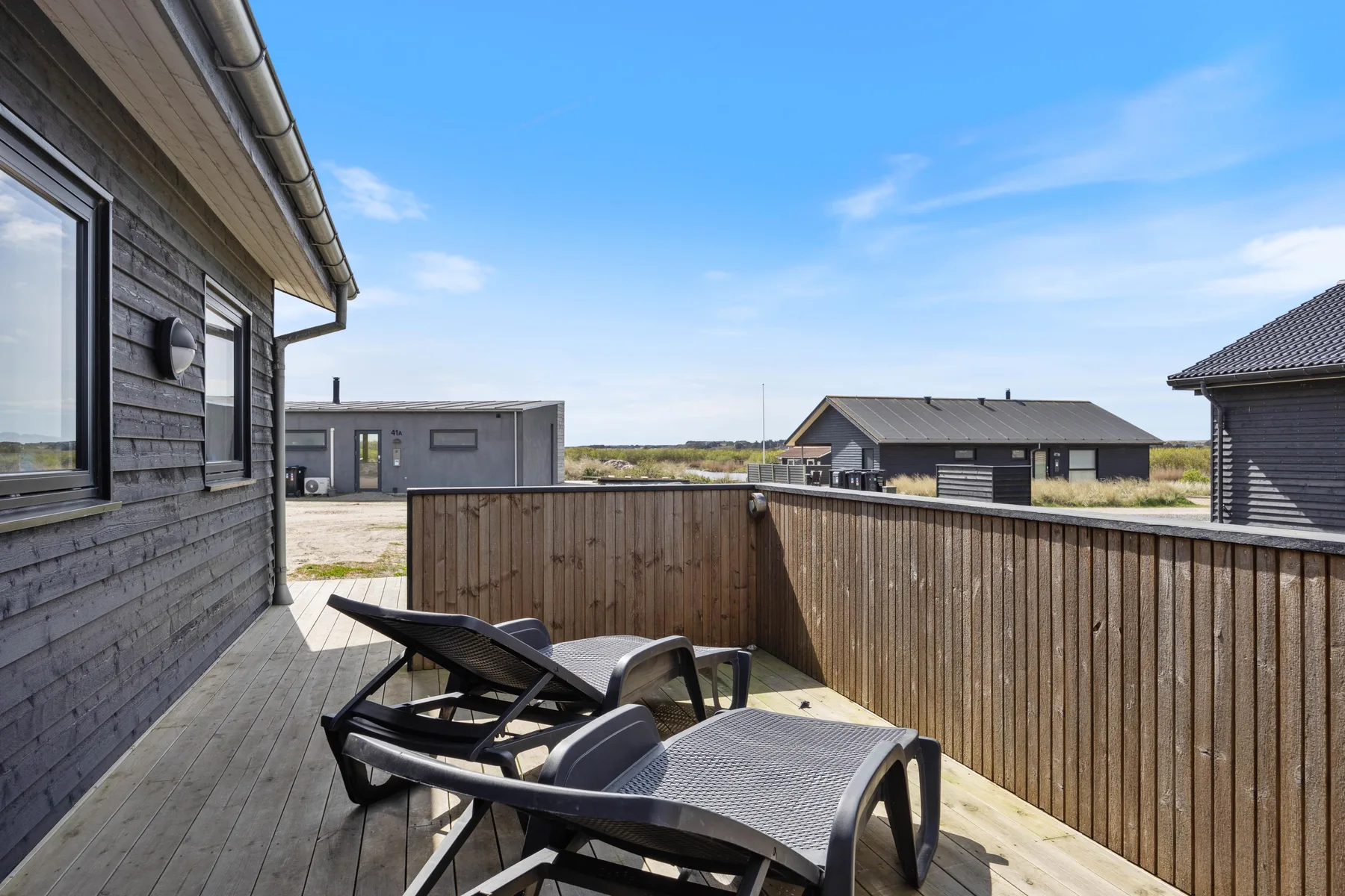 A wooden deck with reclining outdoor seating overlooks nearby houses.