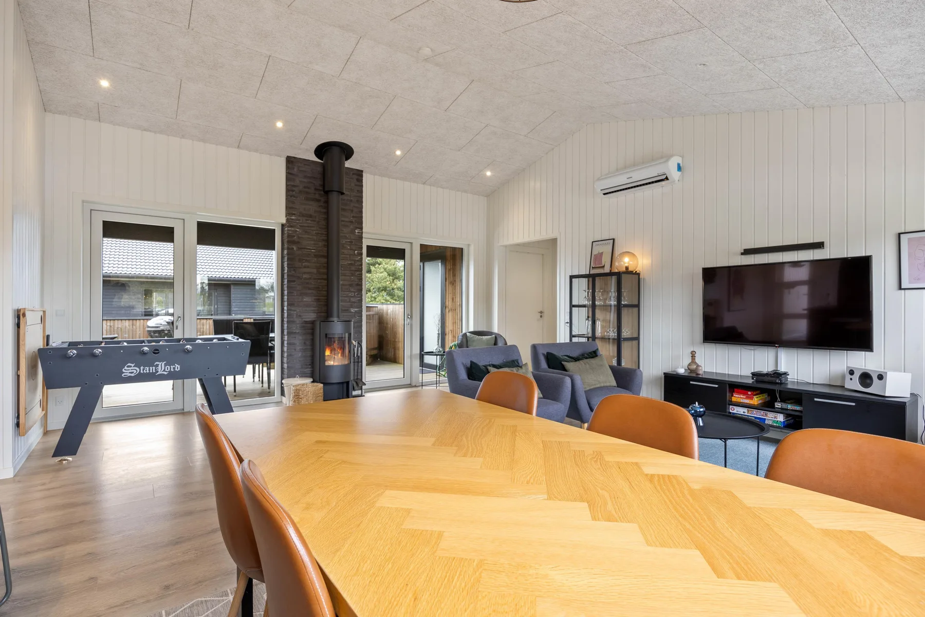 A bright living and dining area features a large table, seating, and a television.