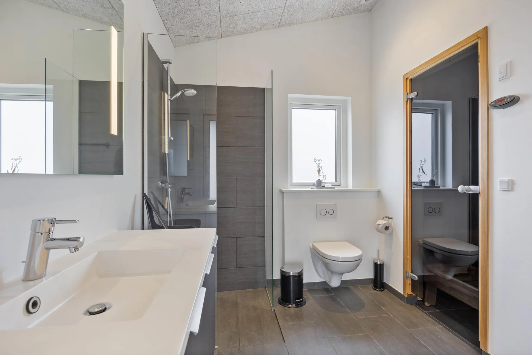 A modern bathroom with a sink, shower, and wall-mounted toilet.