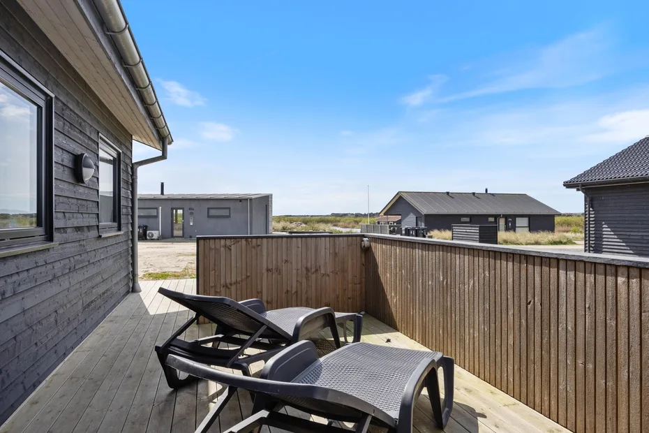 A wooden deck with reclining seating overlooks several low buildings under a clear sky.