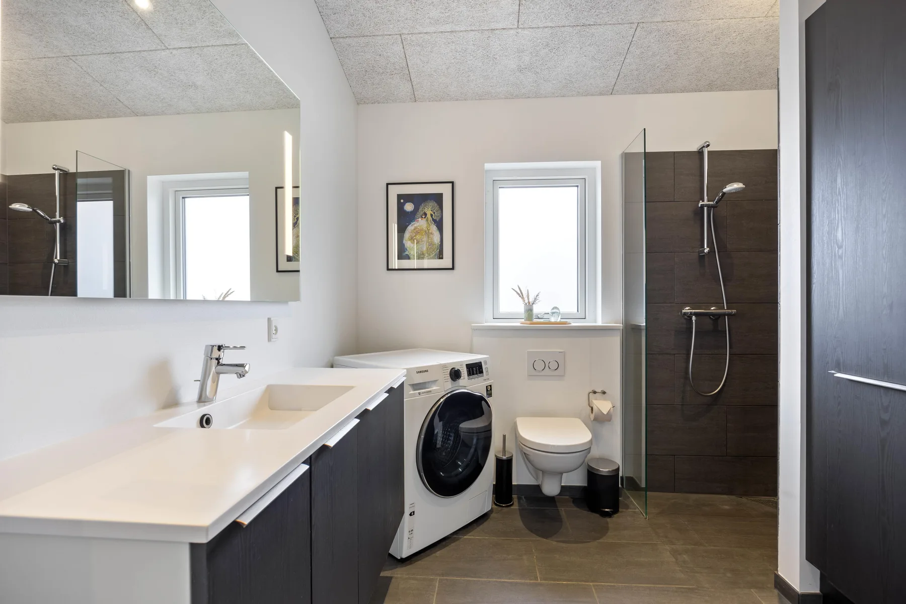 A bathroom with a long vanity, washing machine, toilet, and shower.
