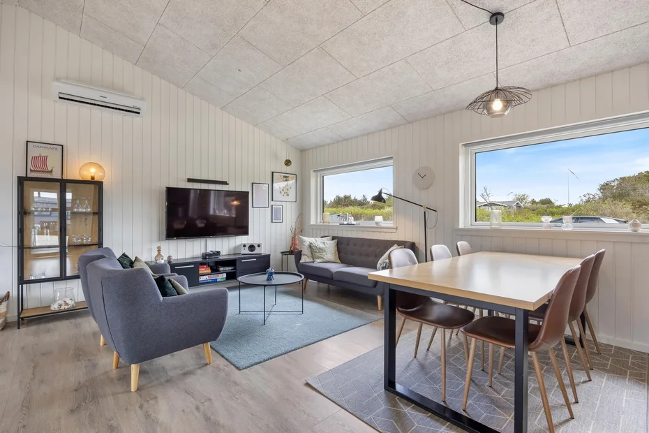 A bright living and dining area with seating, a television, and large windows.