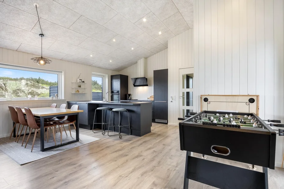 A bright open-plan room with a dining table, kitchen island, and foosball table.