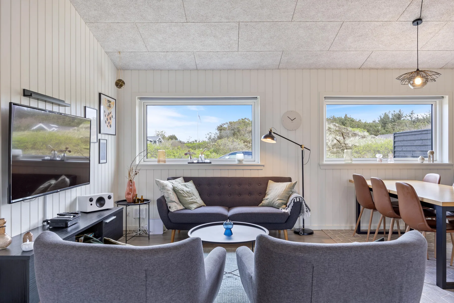 A living room with seating, a television, and a dining table by the windows.