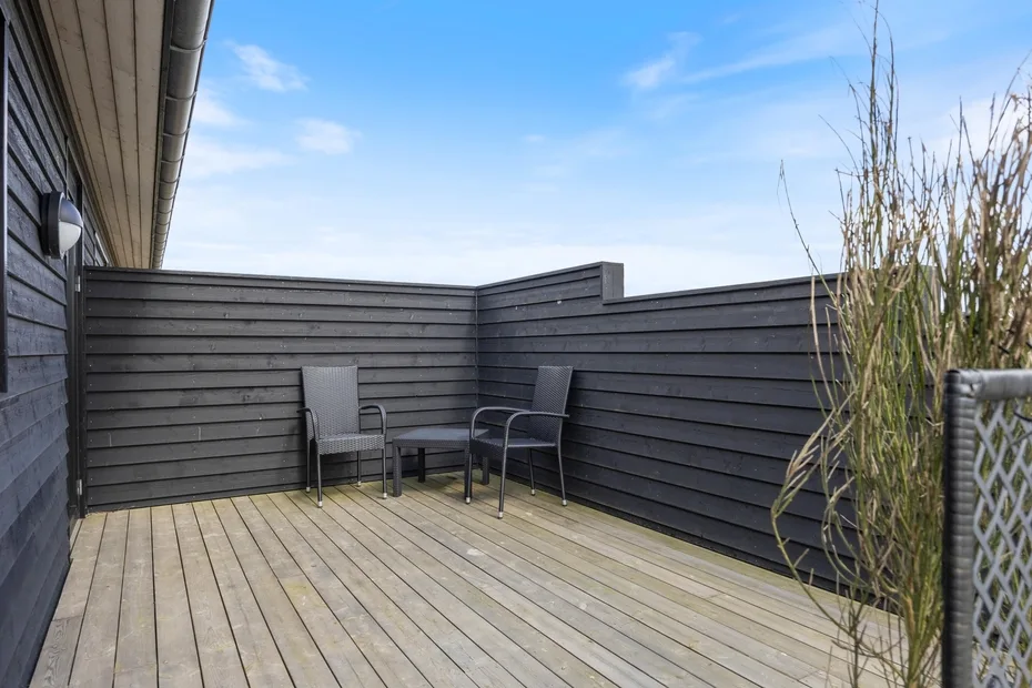 An outdoor deck with seating, enclosed by dark wooden fencing.