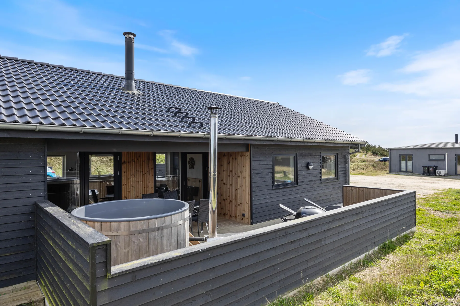 A dark-clad house has a fenced wooden deck with a round hot tub.
