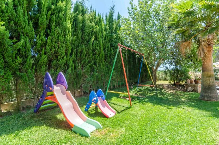 A grassy garden play area with colorful slides and a swing set.