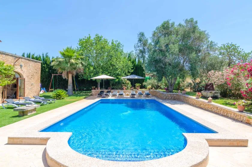 Outdoor swimming pool surrounded by a garden, trees, and lounge seating.