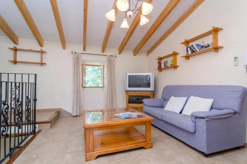 A living room with a sofa, coffee table, and television beneath exposed ceiling beams.