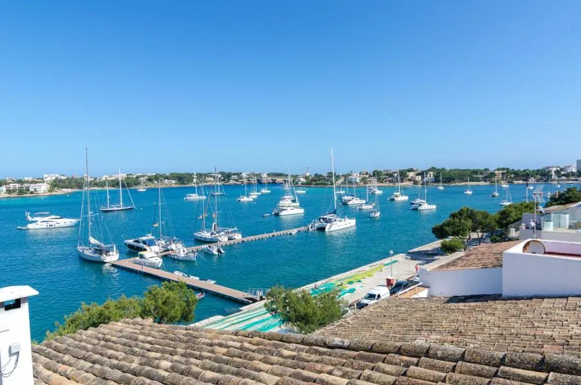 A coastal harbor with sailboats moored in blue water beneath a clear sky.